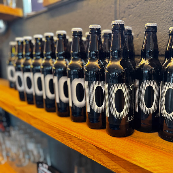 Row of XT Brewing Co XT 10 beer bottles on a wooden shelf in the taproom at XT Brewing Co in Long Crendon