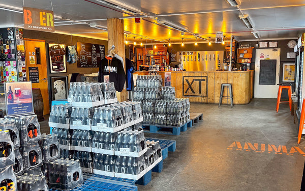 Colour Photo of the XT Brewing Co Taproom in Long Crendon featuring the bar with a big XT logo and pallets of bottled XT beers to the left.