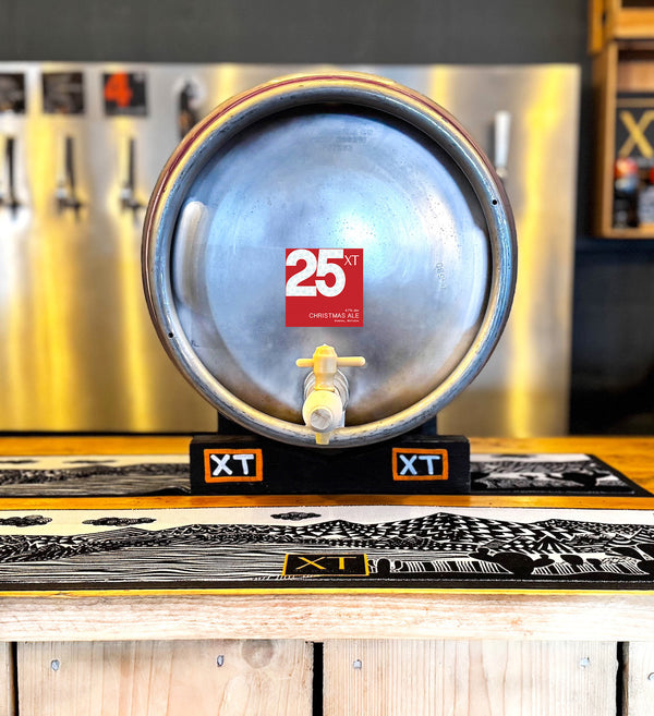 A metal Firkin 72-Pint Cask of XT Brewing Co XT25 Christmas Ale on a tilt on the bar of XT Brewery's Taproom and beer pumps in the background.